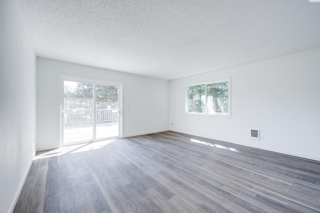 unfurnished room featuring a textured ceiling, visible vents, plenty of natural light, and wood finished floors
