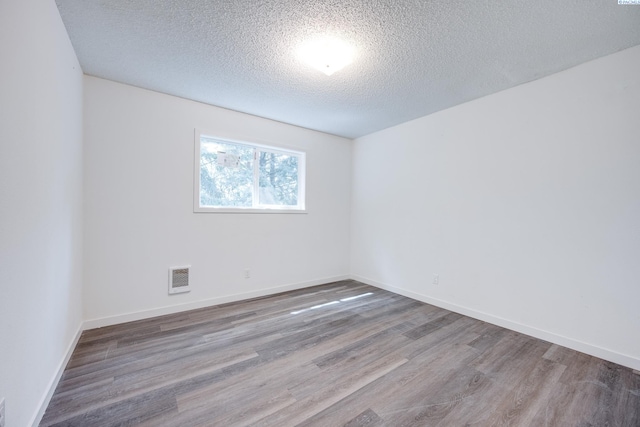 spare room with visible vents, baseboards, a textured ceiling, and wood finished floors