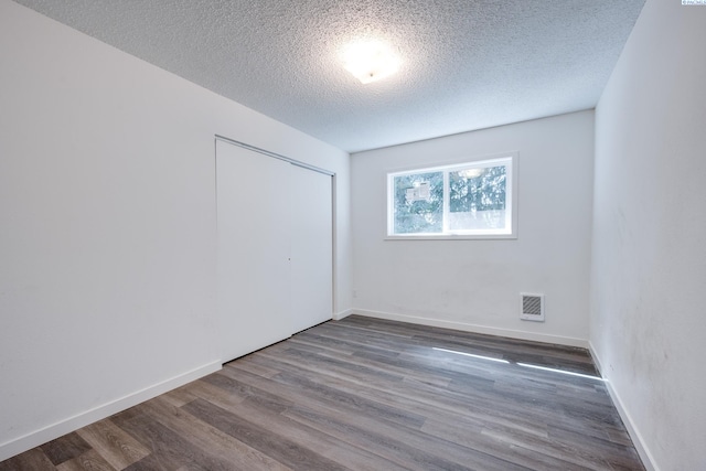 unfurnished bedroom with a textured ceiling, baseboards, visible vents, dark wood-style floors, and a closet