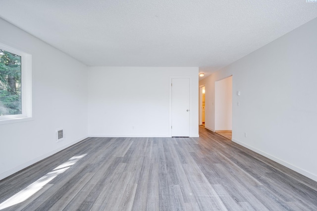 empty room with baseboards, a textured ceiling, wood finished floors, and visible vents