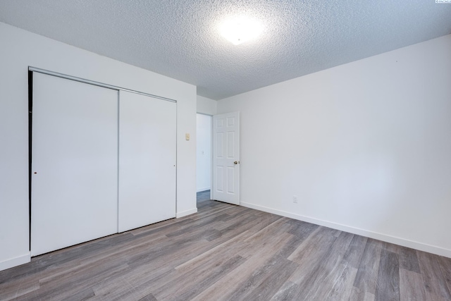 unfurnished bedroom featuring a textured ceiling, baseboards, a closet, and wood finished floors