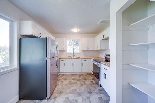 kitchen featuring open shelves, decorative backsplash, white cabinets, stone finish flooring, and stainless steel appliances
