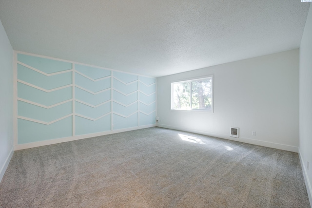 empty room with carpet floors, a textured ceiling, baseboards, and visible vents