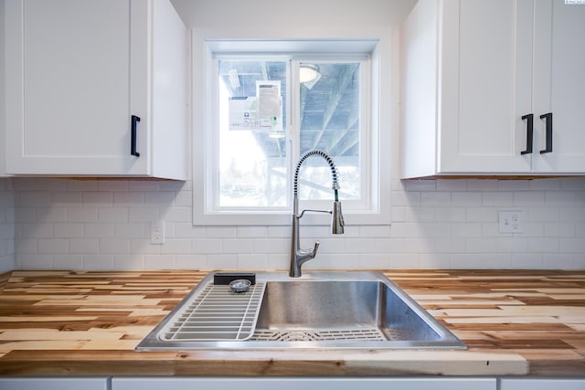 kitchen with a sink, white cabinets, tasteful backsplash, and butcher block countertops