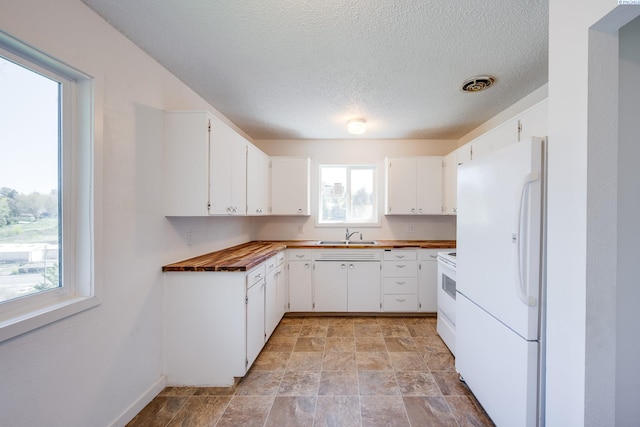 kitchen featuring stone finish floor, a textured ceiling, visible vents, a sink, and white appliances