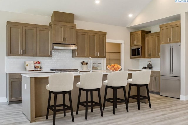 kitchen featuring a breakfast bar, a kitchen island with sink, backsplash, stainless steel appliances, and vaulted ceiling