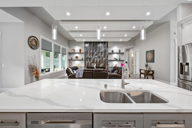 kitchen with light stone counters, a sink, open floor plan, hanging light fixtures, and appliances with stainless steel finishes