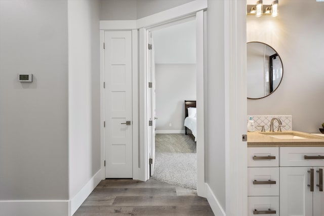 bathroom featuring baseboards, connected bathroom, wood finished floors, vanity, and backsplash