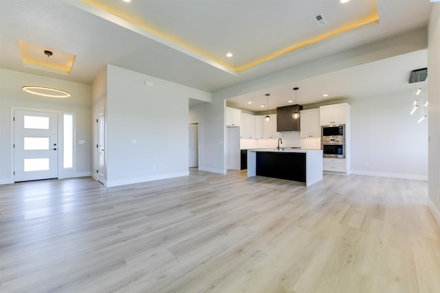 unfurnished living room featuring a raised ceiling, sink, and light hardwood / wood-style floors