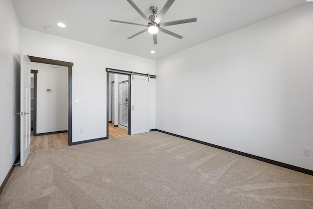 unfurnished bedroom with a barn door, light colored carpet, and ceiling fan