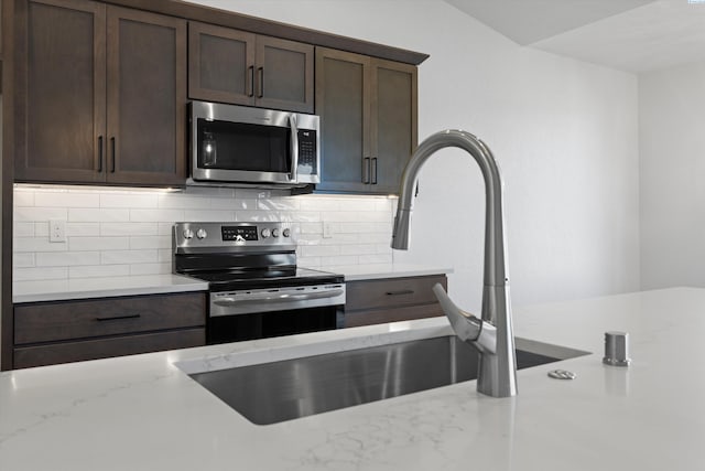 kitchen with appliances with stainless steel finishes, tasteful backsplash, sink, light stone counters, and dark brown cabinets