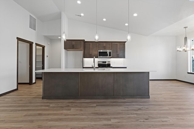 kitchen featuring dark brown cabinetry, a center island with sink, pendant lighting, stainless steel appliances, and light hardwood / wood-style floors