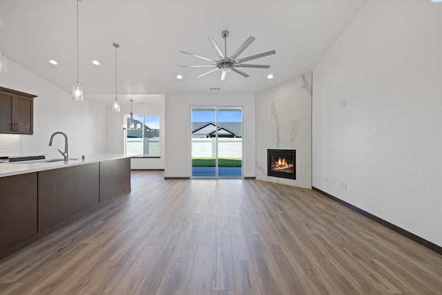 unfurnished living room featuring ceiling fan, a fireplace, sink, and light wood-type flooring