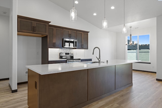 kitchen featuring a kitchen island with sink, sink, decorative light fixtures, and appliances with stainless steel finishes