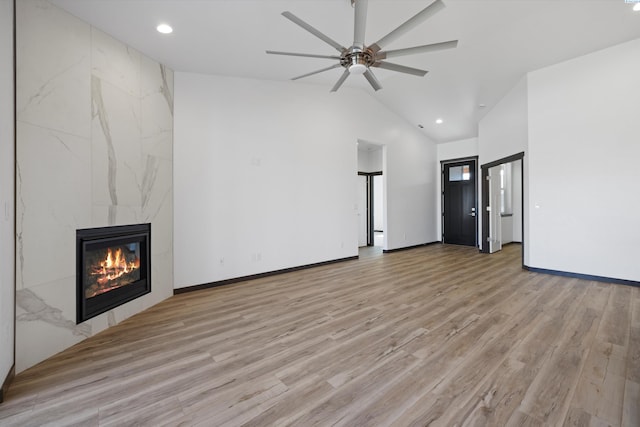 unfurnished living room with ceiling fan, a premium fireplace, high vaulted ceiling, and light wood-type flooring