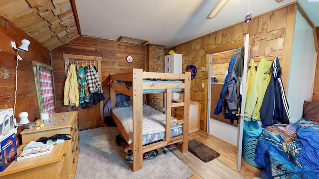 bedroom featuring lofted ceiling, wooden walls, and wood finished floors