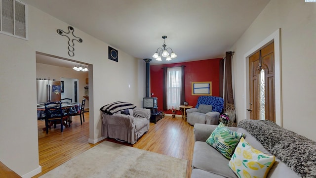 living room featuring a wood stove, visible vents, an inviting chandelier, and wood finished floors