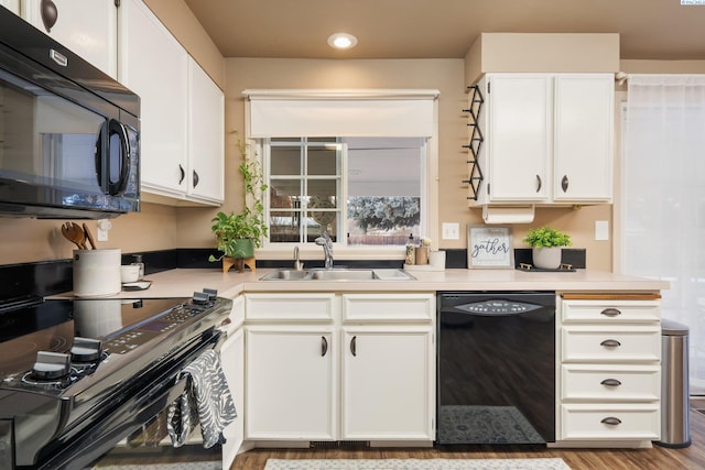 kitchen with a sink, black appliances, light countertops, white cabinetry, and recessed lighting