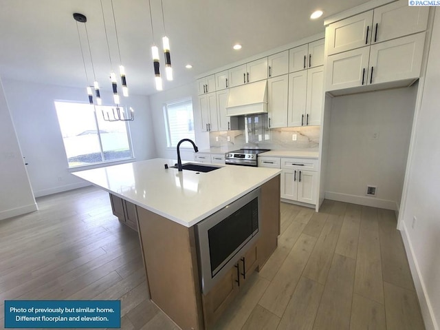 kitchen featuring white cabinetry, an island with sink, custom range hood, and built in microwave