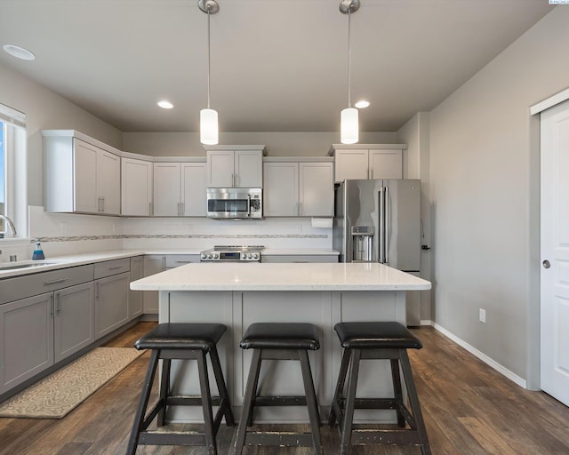 kitchen with a kitchen island, appliances with stainless steel finishes, a breakfast bar area, gray cabinetry, and backsplash