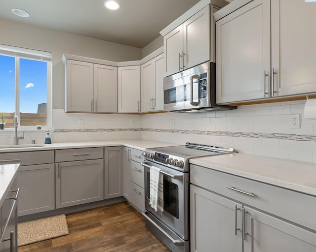 kitchen with stainless steel appliances, a sink, backsplash, gray cabinets, and dark wood-style floors