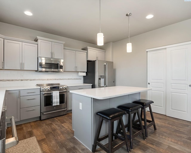 kitchen with dark wood-style floors, a breakfast bar, light countertops, gray cabinetry, and appliances with stainless steel finishes