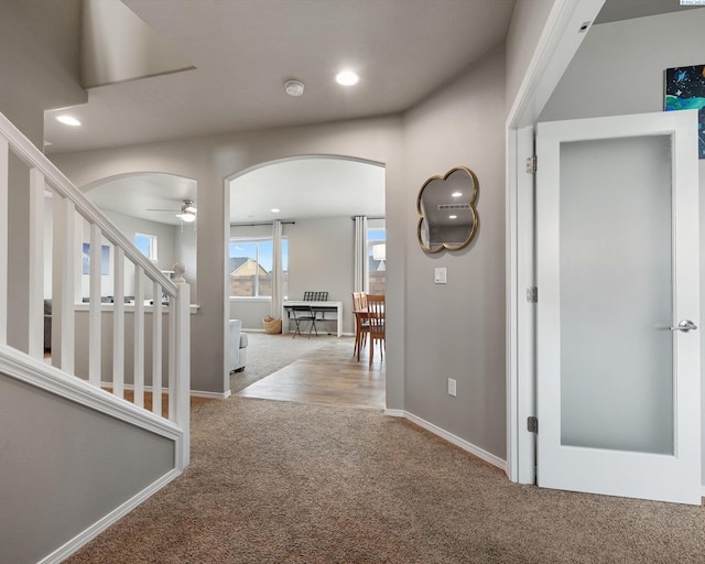 hallway featuring arched walkways, recessed lighting, carpet flooring, baseboards, and stairs