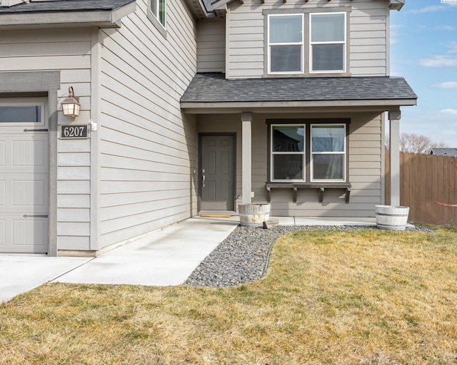 entrance to property with a garage, a yard, a shingled roof, and fence