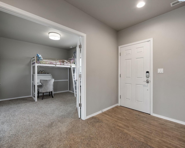 carpeted entrance foyer with baseboards, visible vents, and wood finished floors