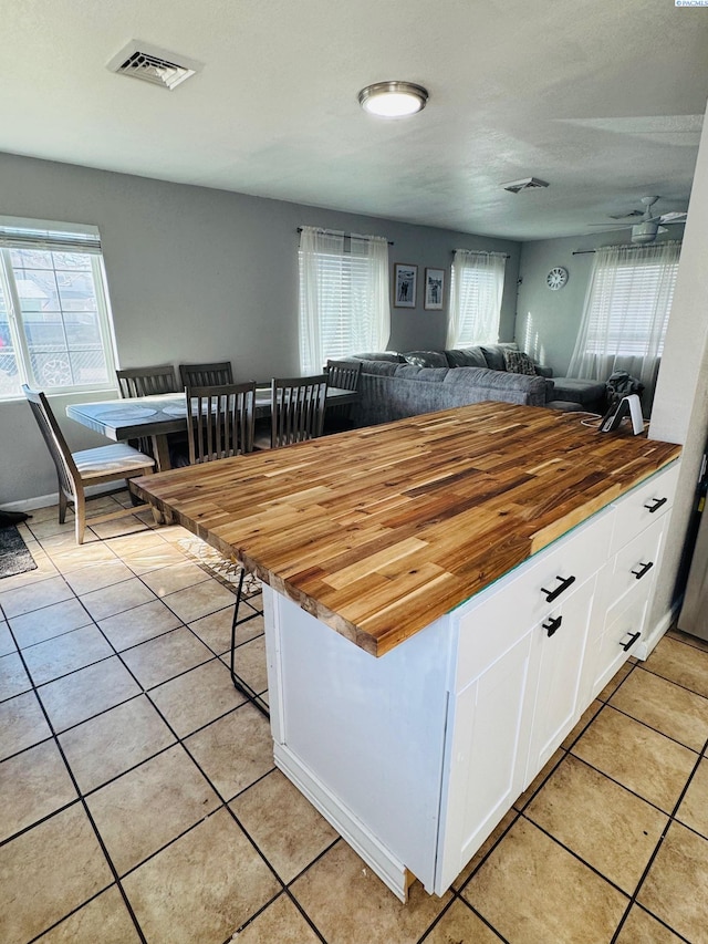 kitchen with light tile patterned floors, white cabinetry, butcher block countertops, and visible vents