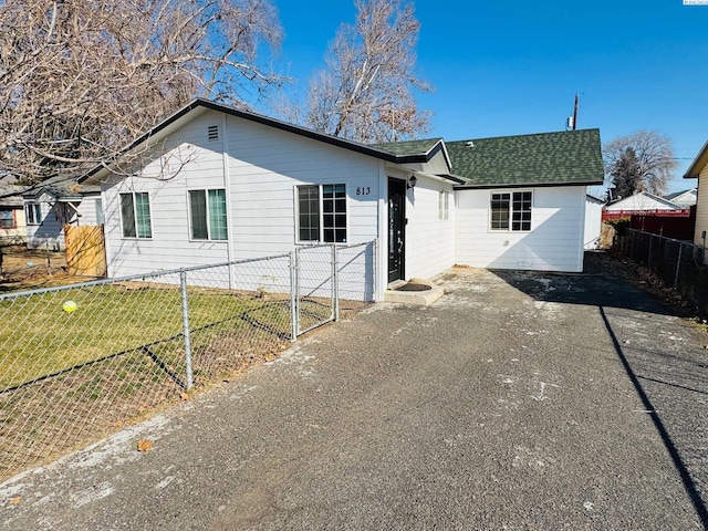 view of front facade with fence private yard, roof with shingles, driveway, and a front yard