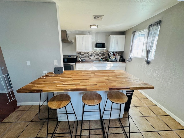 kitchen with visible vents, decorative backsplash, stainless steel range with electric stovetop, black microwave, and wall chimney exhaust hood