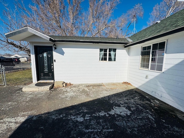 property entrance with roof with shingles and fence