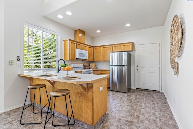4611 Arabian Ln, Pasco, WA 99301 - kitchen featuring white appliances, a peninsula, light countertops, recessed lighting, and a kitchen bar