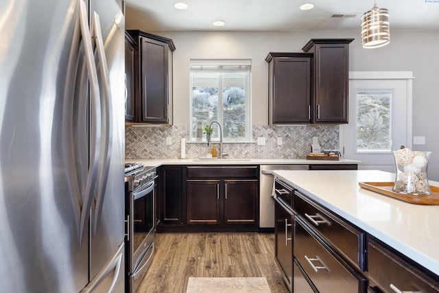 kitchen with light countertops, appliances with stainless steel finishes, a sink, and decorative light fixtures