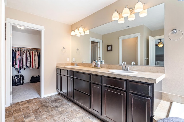 full bathroom with double vanity, a sink, a walk in closet, and baseboards