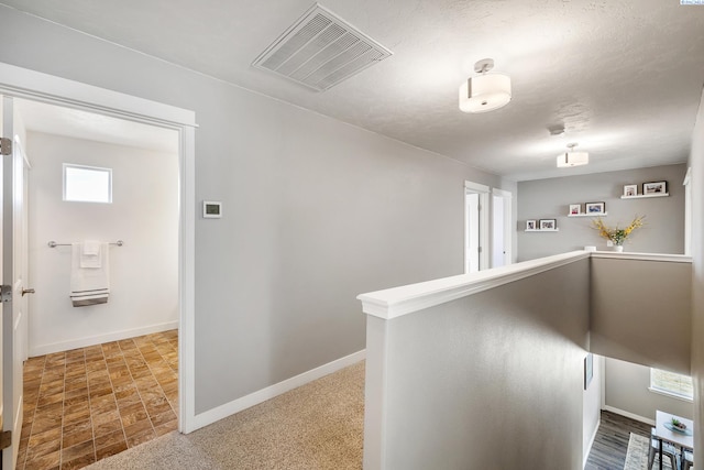 hallway featuring a textured ceiling, an upstairs landing, visible vents, baseboards, and carpet