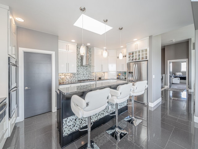5880 S 58th Ave, West Richland, WA 99353 - kitchen featuring stainless steel appliances, a skylight, wall chimney exhaust hood, a breakfast bar area, and light stone countertops