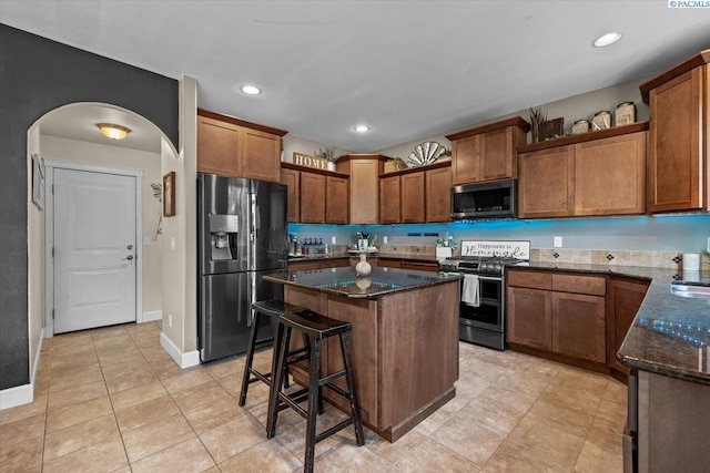 5200 W 28th Ave, Kennewick, WA 99338 - kitchen featuring appliances with stainless steel finishes, dark stone countertops, a kitchen island, brown cabinetry, and arched walkways