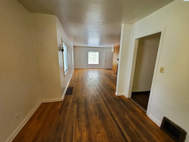 corridor with baseboards, visible vents, and dark wood-type flooring