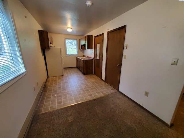 kitchen featuring a sink, baseboards, freestanding refrigerator, and light countertops