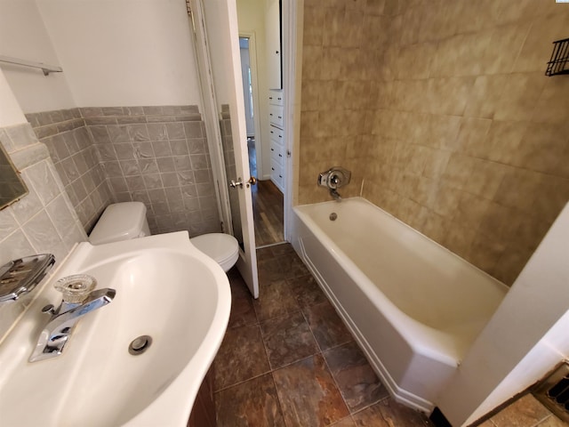 full bathroom featuring a sink, tile walls, a bathing tub, and toilet