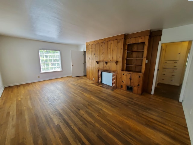 unfurnished living room with baseboards, a brick fireplace, and wood finished floors