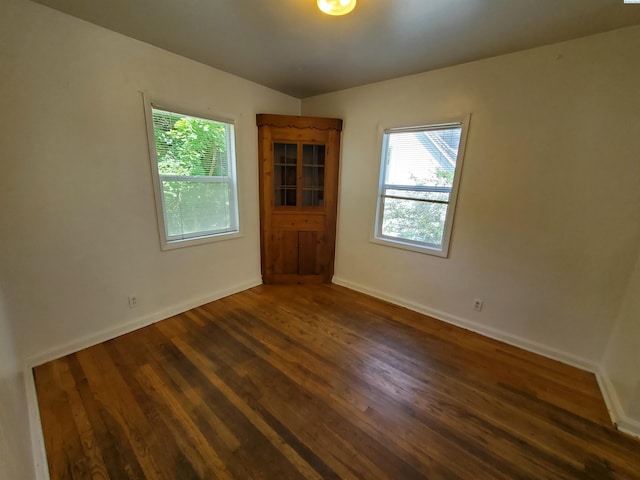 unfurnished room featuring baseboards, a wealth of natural light, and dark wood-type flooring