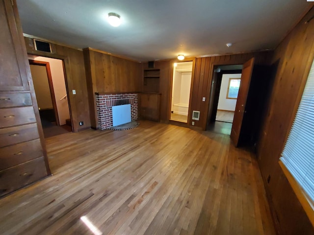 unfurnished living room with wood-type flooring, a brick fireplace, wood walls, and visible vents