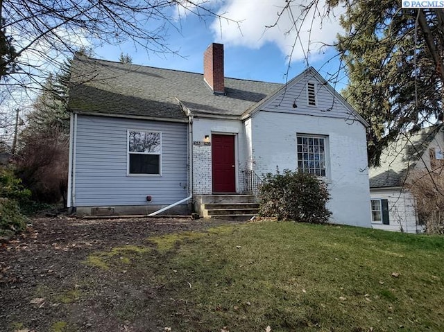 rear view of house featuring a lawn, a chimney, and roof with shingles