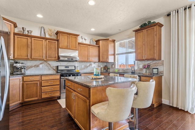 5601 Santa Fe Ln, Pasco, WA 99301 - kitchen featuring under cabinet range hood, stainless steel gas range, brown cabinetry, and dark wood-style flooring