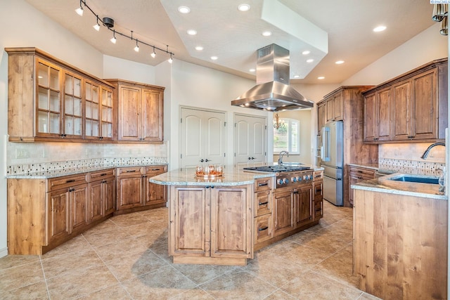 kitchen with appliances with stainless steel finishes, a sink, island range hood, backsplash, and a center island with sink