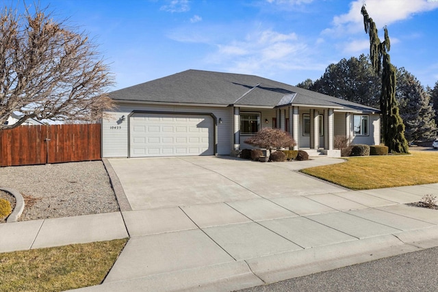 view of front of home with a front yard, fence, roof with shingles, an attached garage, and concrete driveway