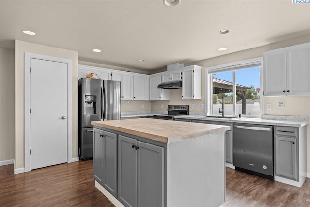 kitchen with stainless steel appliances, under cabinet range hood, wood counters, dark wood-style floors, and a sink